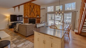 A spacious living room with a fireplace, a large TV, and a dining area with a wooden table and chairs. - Shuttle to Loon, Hot Tub & Pool! (Lincoln)