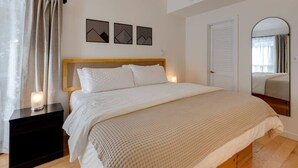 A neatly made bed with a wooden headboard, a bedside table with a candle, and a wall with three geometric wall art pieces. - Shuttle to Loon, Hot Tub & Pool! (Lincoln)