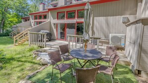 A two-story house with a red and white exterior, a covered patio with wicker furniture, and a staircase leading to the upper floor. - Shuttle to Loon, Hot Tub & Pool! (Lincoln)
