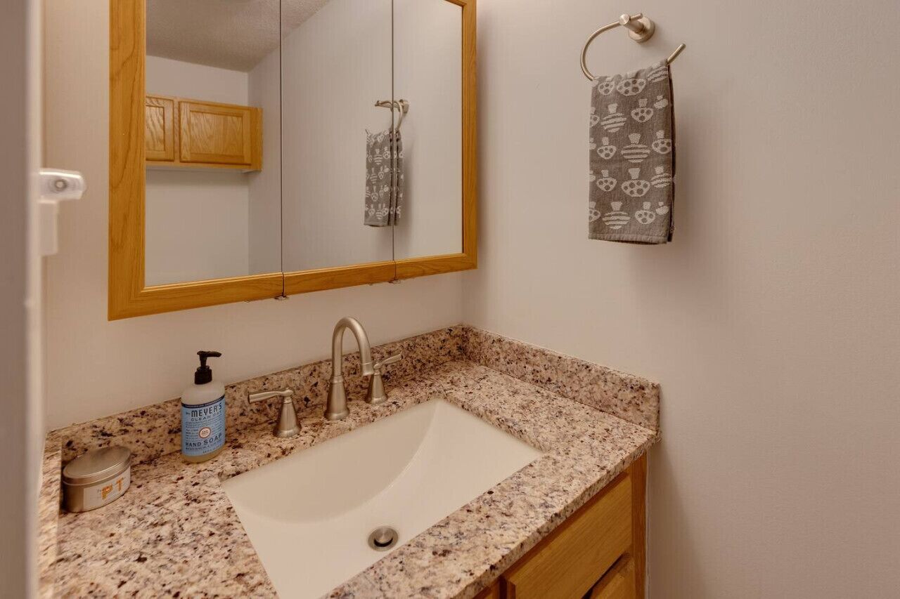 A bathroom with a granite countertop sink, a mirror, a towel rack with a patterned towel, and a bottle of hand soap.