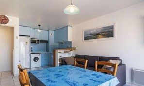 A compact kitchen with a washing machine, a dining table with chairs, and a sofa.