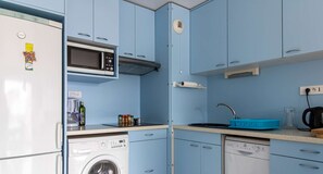 Efficient kitchen with microwave, washing machine, and dishwasher, plus a coffee maker and blue cutting board.