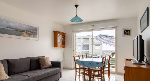 Relax in this stylish living room with a sofa, dining table for four, and a large window offering a view of the surrounding building.