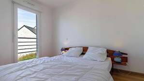 A bedroom with a bed, two bedside lamps, a window, and a view of a building outside. - Bright apartment with terrace in Erquy | 4 guests | Ref 531 (ERQUY)