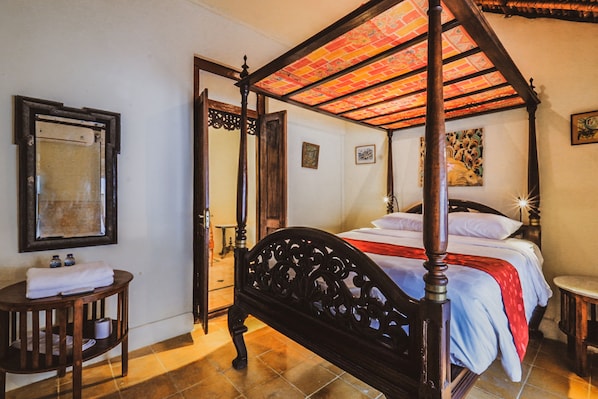 Una cama con dosel rojo, cabecera de madera y mesita de noche con una toalla y una botella.