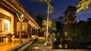 A traditional building with a thatched roof, a stone statue, and a small pond. - Bebek Cottages Sanur (Denpasar)