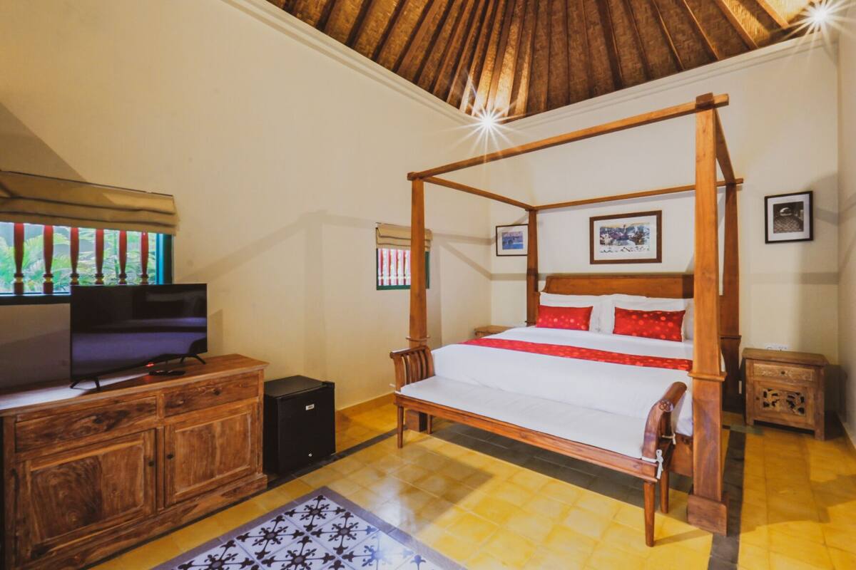 A four-poster bed with a wooden frame, a television on a wooden cabinet, and a small speaker.