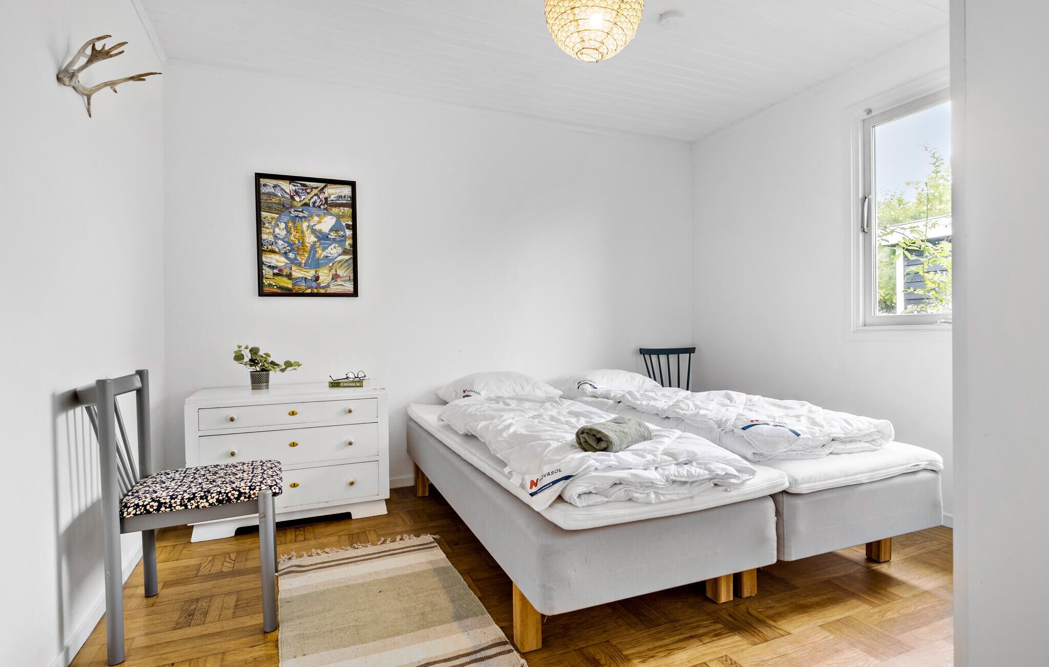 Een slaapkamer met twee bedden, een kaptafel, een stoel, een vloerkleed, een schilderij en een raam.