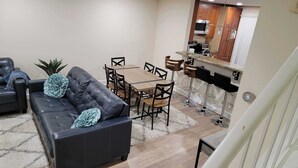 A compact living space with a black leather sofa, a wooden dining table, and a kitchen area with a microwave and toaster. - Premium Modern TH • Near Dulles Airport • 2 Free Parking (Clifton)