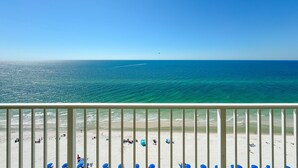 Strandudsigt fra en balkon med gelænder, hav og mennesker på stranden.