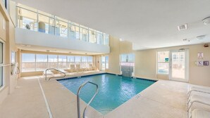 En indendørs swimmingpool med et glasloft, liggestole og udsigt til det fri.