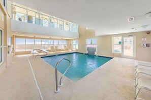 Ein Hallenbad mit Glasgeländer, Liegestühlen und Blick ins Freie.