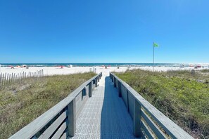 A wooden boardwalk leading to a beach with a flag on a pole. - Shoalwater 303 | Gorgeous Beachfront Condo | Indoor, Outdoor Pools, Tennis, Sauna, Gym (Orange Beach)