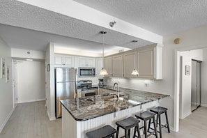 A modern kitchen with a marble island, stainless steel appliances, and pendant lighting. - Shoalwater 303 | Gorgeous Beachfront Condo | Indoor, Outdoor Pools, Tennis, Sauna, Gym (Orange Beach)