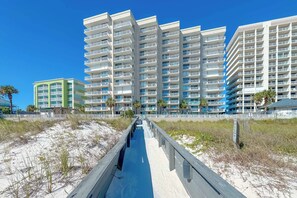A beachfront hotel with multiple floors, a boardwalk leading to the beach, and palm trees. - Shoalwater 303 | Gorgeous Beachfront Condo | Indoor, Outdoor Pools, Tennis, Sauna, Gym (Orange Beach)