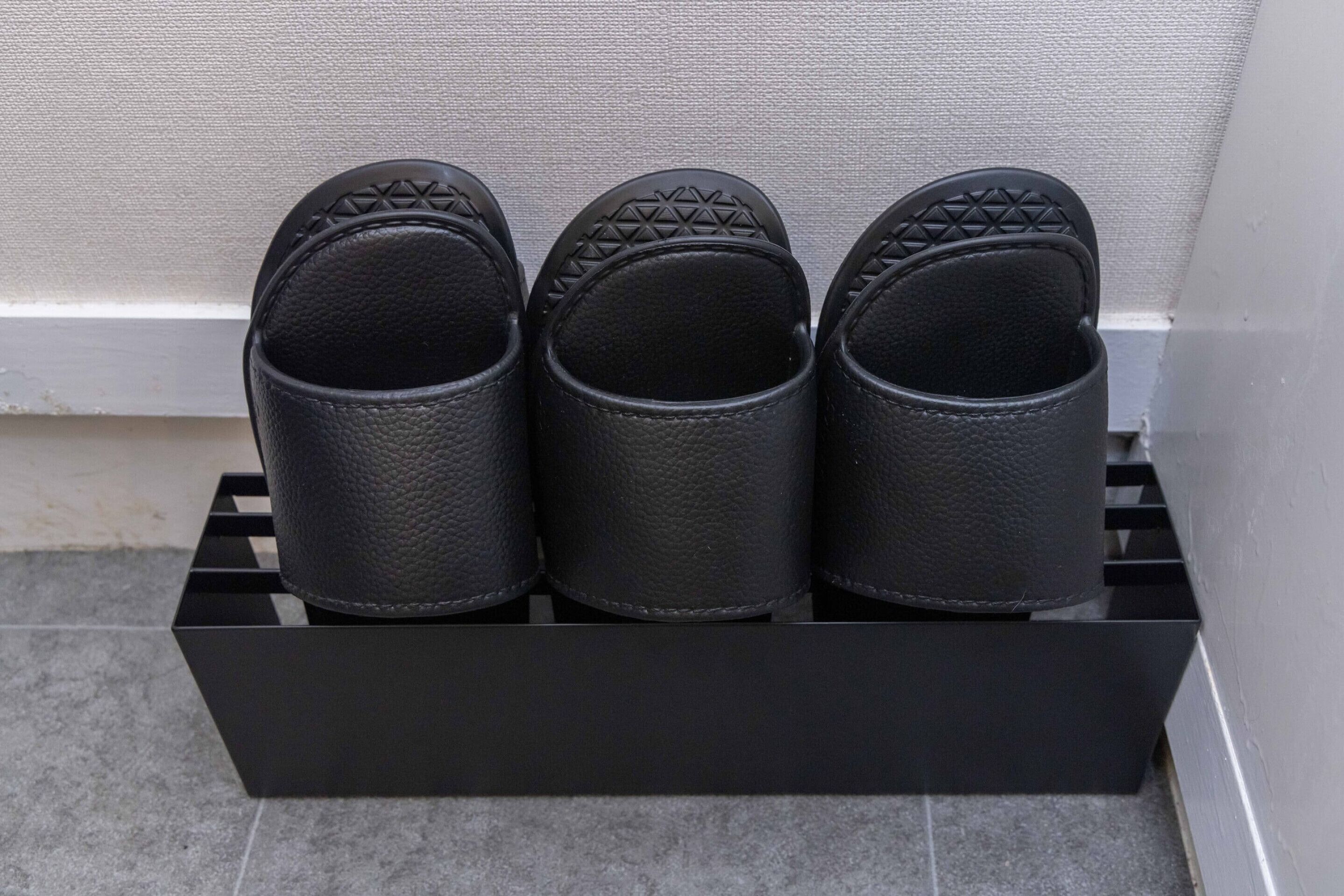 Un porte-chaussures noir contenant trois paires de chaussures noires.