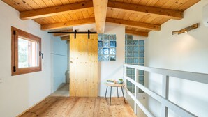 Een kamer met houten vloer, houten plafond, een raam met houten kader en een witte leuning.