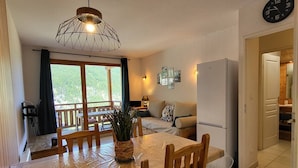 A dining area with a wooden table and chairs, a hanging light fixture, and a view of the outdoors through a window. - N°609 Balcon des Airelles (LES ORRES 1800)