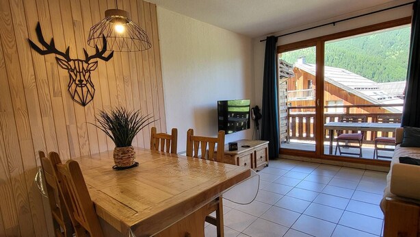 A dining area with a wooden table and chairs, a wall-mounted deer head decoration, and a TV on a wooden cabinet. - N°609 Balcon des Airelles (LES ORRES 1800)