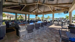 An outdoor patio area with a bar, seating, and a pool in the background. - Resort-style 1st Floor Condo in Lakewood National Golf Community-Lakewood Ranch! (Lakewood Ranch)