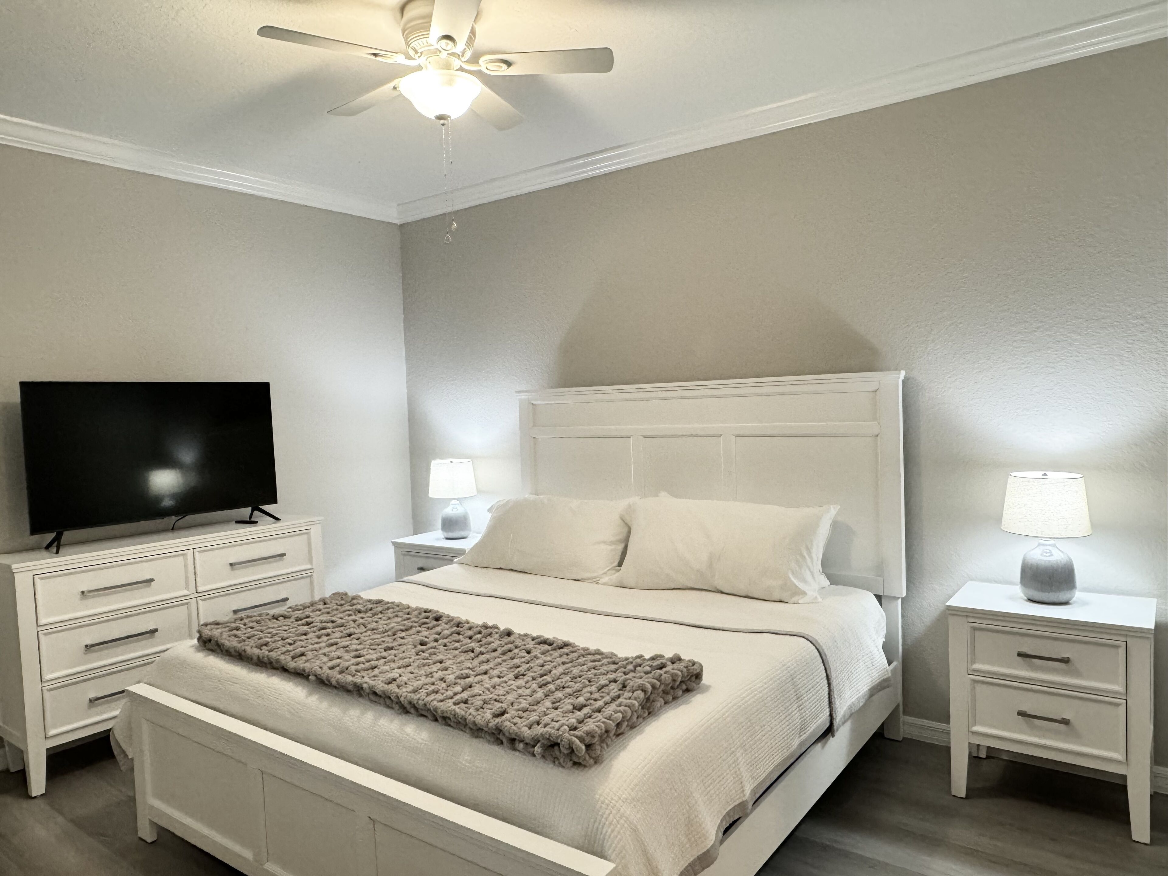 A bedroom with a bed, a TV, two bedside tables, and a ceiling fan.