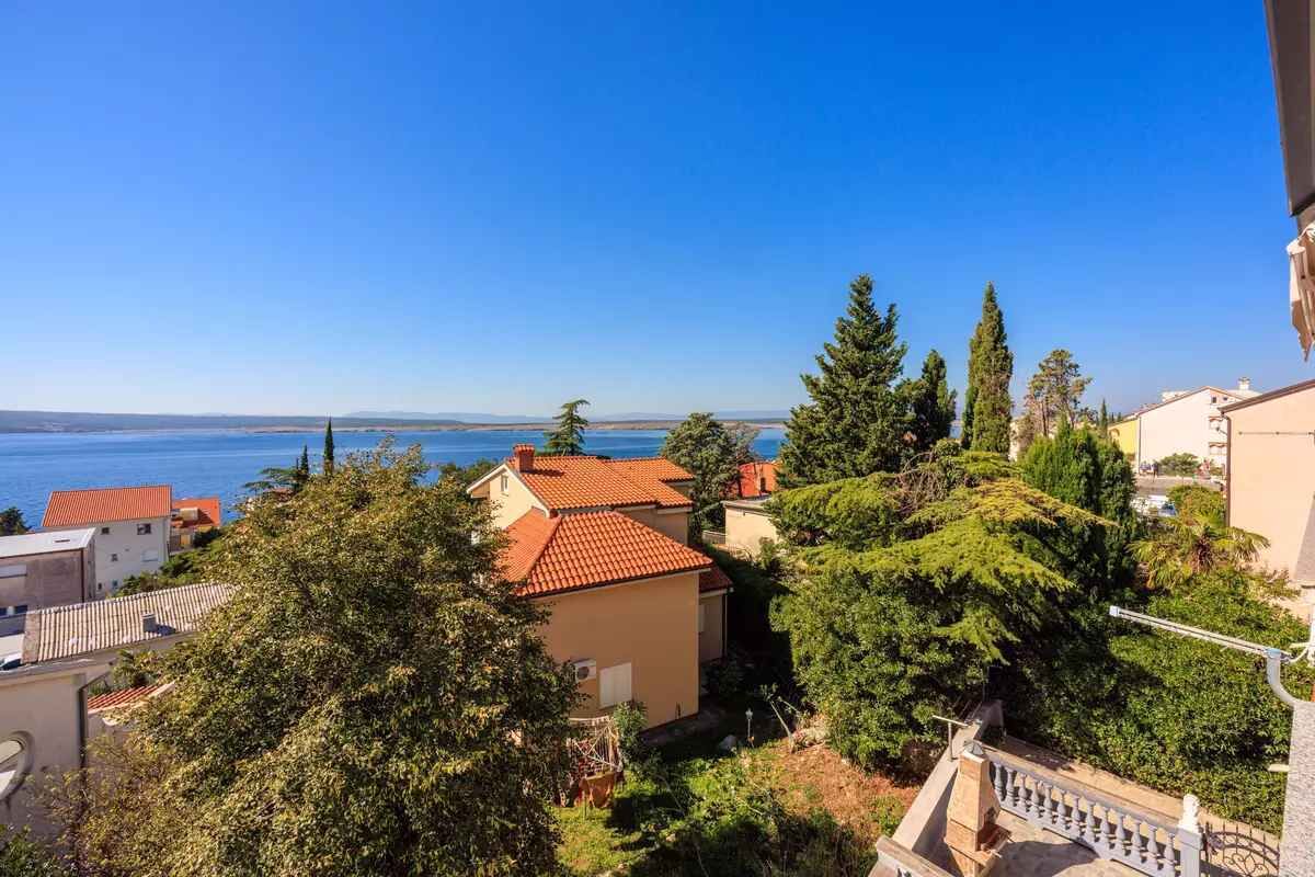 A coastal residential area with houses, trees, and a clear view of the sea.
