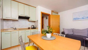 A compact kitchen with light green cabinets, a wooden dining table with yellow chairs, and a potted plant on the table. - Holiday apartment with a nice balcony (Dramalj)