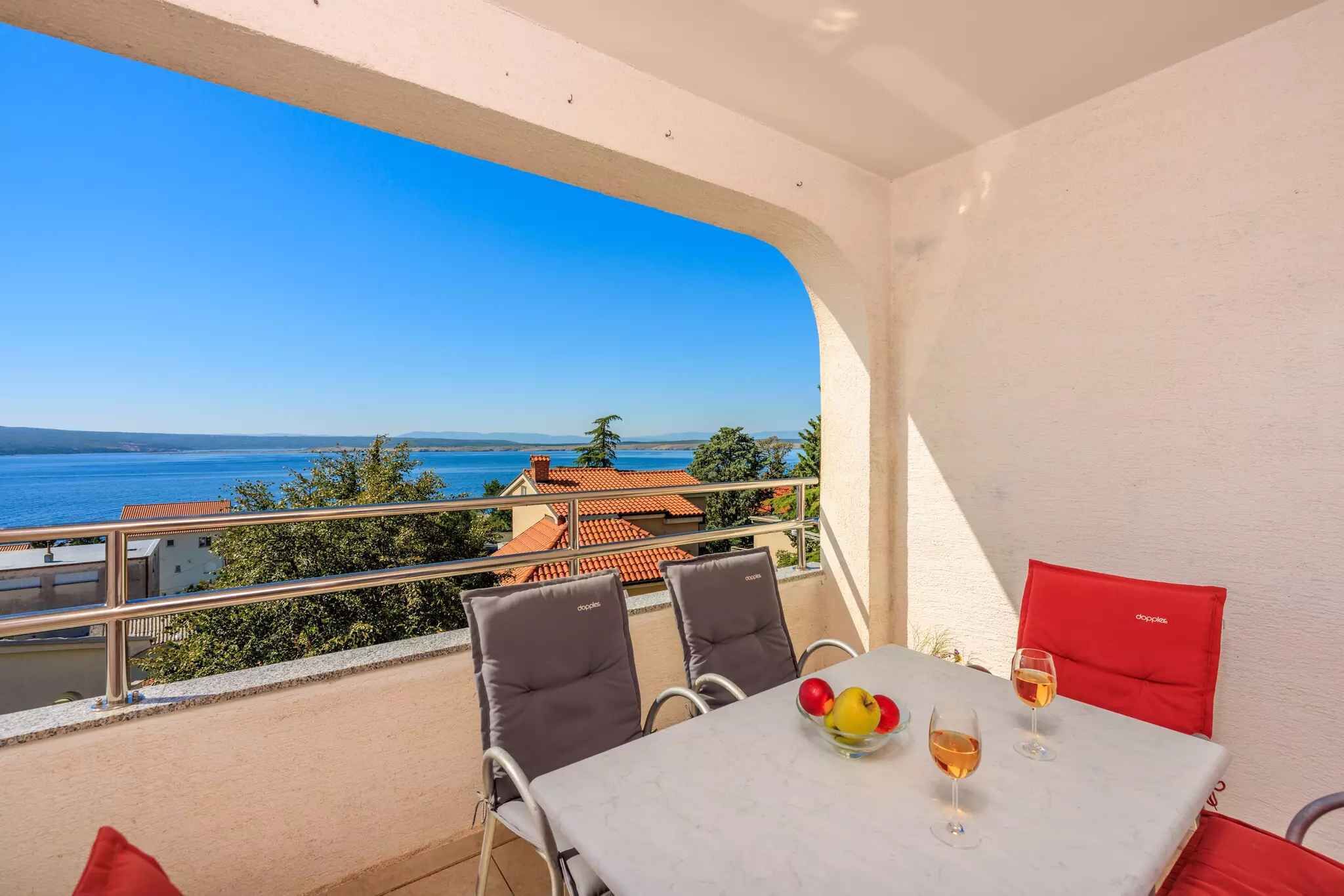 A balcony with a table, chairs, and a view of the sea.