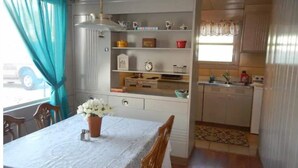 Een compacte keuken met een eethoek, voorzien van een tafel met een witte tafelkleed, een potplant en een raam met gordijnen.