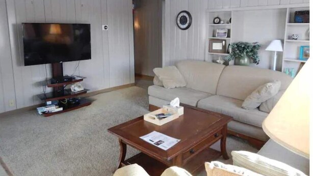 Een woonkamer met een televisie, bank, salontafel en planken met decoratieve objecten.