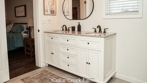 A bathroom with a white vanity, a round mirror, and a window with blinds.