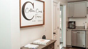 A kitchen with a microwave, coffee maker, and a dishwasher. There is a framed sign on the wall and a small table with books.