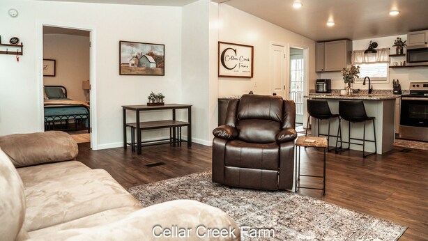 A spacious living room with a leather recliner, a dining area with a small table, and a kitchen with bar stools.