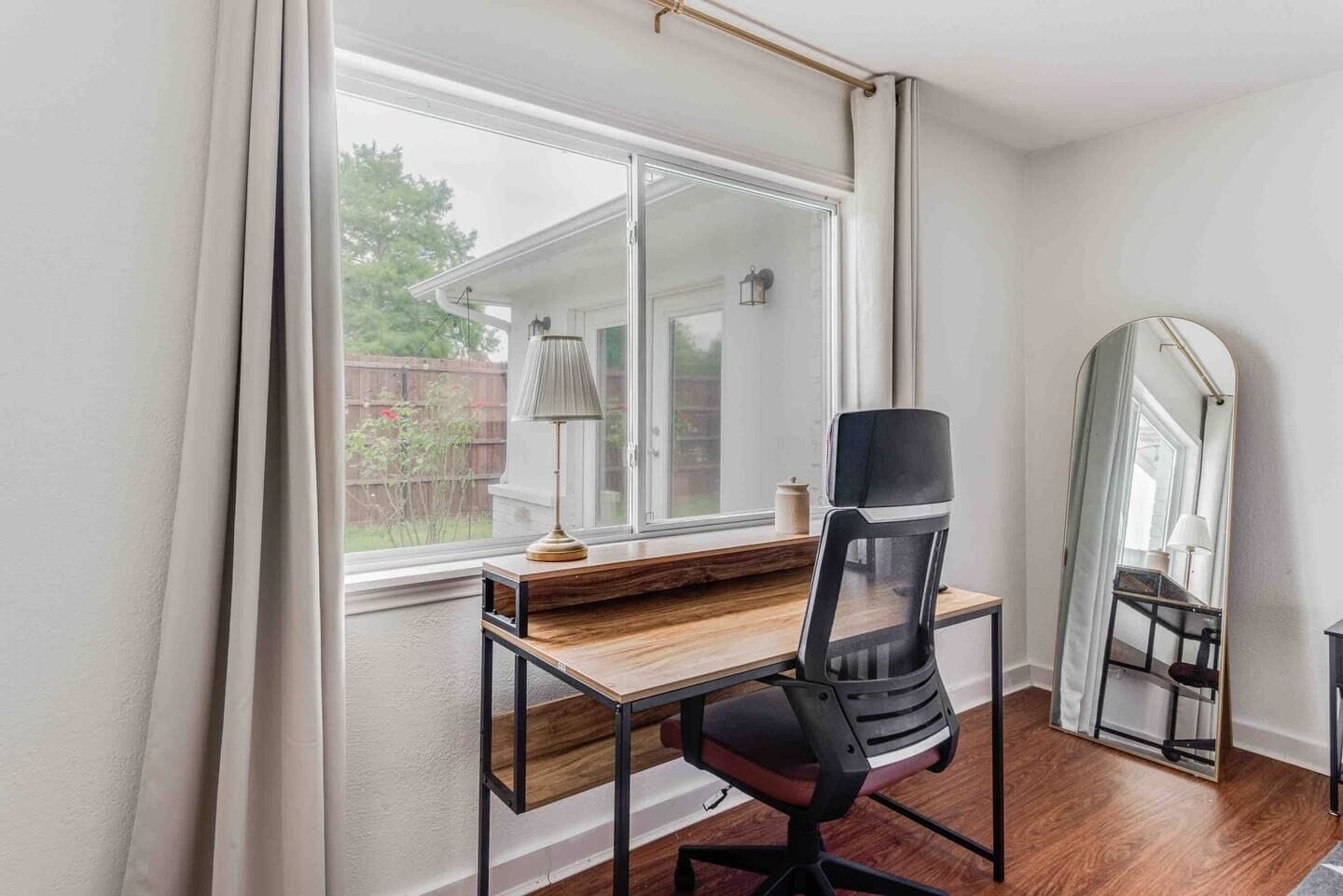 A room with a desk, chair, and a large mirror.
