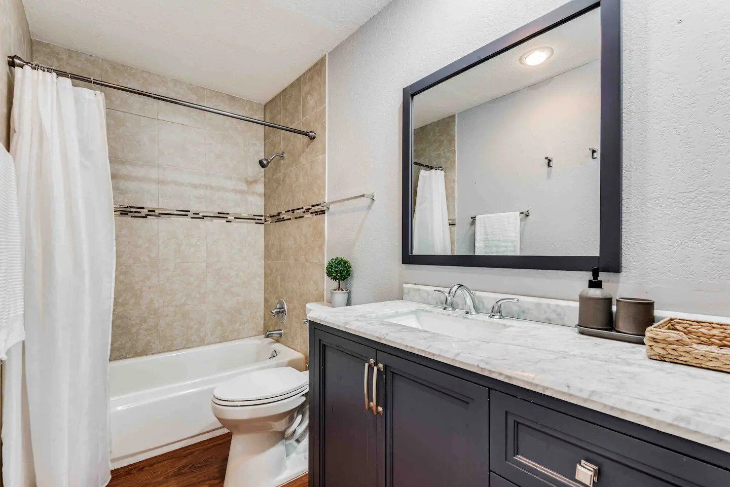 A bathroom with a bathtub, toilet, and a large mirror above the sink.