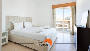 Habitación de hotel con una cama grande, televisión, escritorio y balcón con vistas a la ciudad.