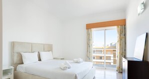 Habitación de hotel con una cama grande, televisión, escritorio y balcón con vistas a la ciudad.