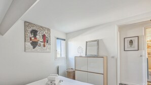A bedroom with a bed, a radiator, a window, a mirror, and artwork on the walls.