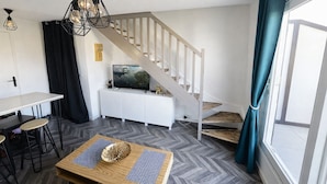 A modern living room with a staircase, a dining area, and a view through a window.