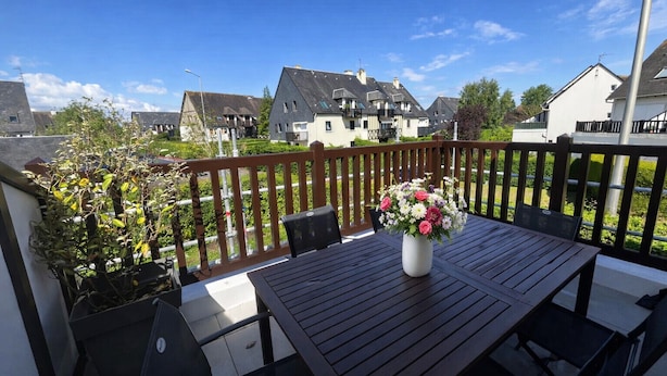 A balcony with a table and chairs, a flower vase, and a view of houses.