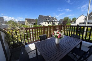 Un balcon avec une table et des chaises, un vase de fleurs et une vue sur les maisons.