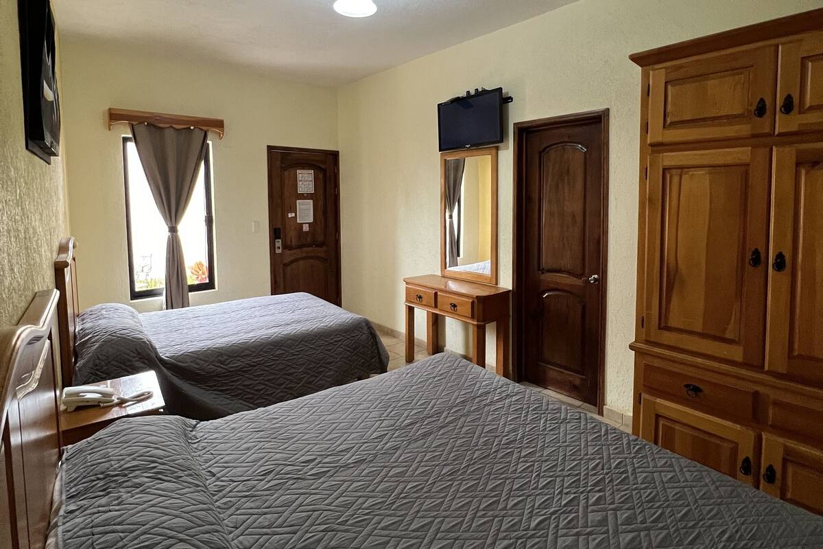 A bedroom with two beds, wooden wardrobe, a desk, and a mirror.