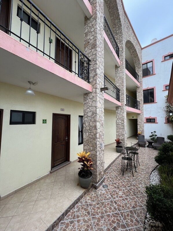 A multi-story building with a stone facade, balconies with metal railings, and a tiled patio area with outdoor furniture. - Hotel La Capilla Bernal (Ezequiel Montes)