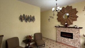Una sala de estar con chimenea, dos sillones, una mesita con flores y decoración en la pared.