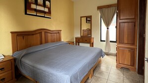 Un dormitorio con cama de madera, una mesita de noche, un aparador, un espejo y una lámpara en el techo.