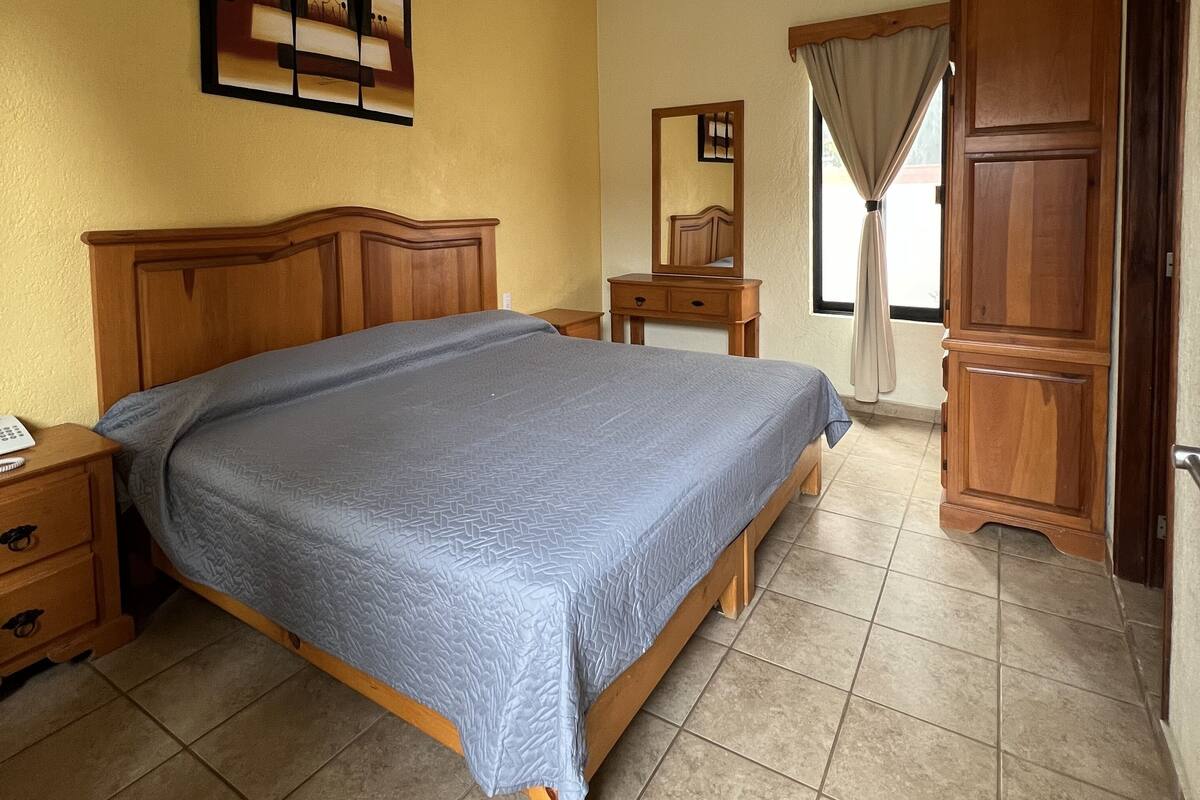 A bedroom with a wooden bed, a nightstand, a dresser, a mirror, and a ceiling light.