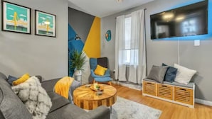 Ein modernes Wohnzimmer mit Sofa, Sessel, Couchtisch und einem an der Wand befestigten Fernseher.