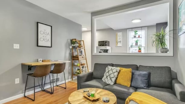 Ein modernes Wohnzimmer mit einem grauen Sofa, einem Holztisch und einem Essbereich mit Schreibtisch und Stühlen.