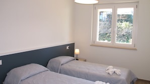 Ett sovrum med två sängar, ett fönster med utsikt över träd, en lampa och en taklampa.