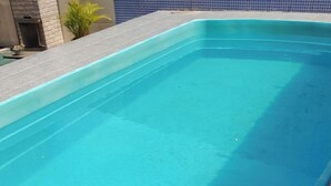 En swimmingpool med flisekant og en stenvæg i baggrunden.